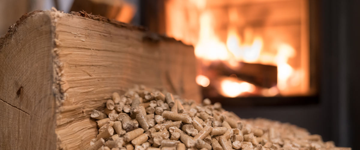 Holzstück und Holzpellets vor einem Kaminfeuer